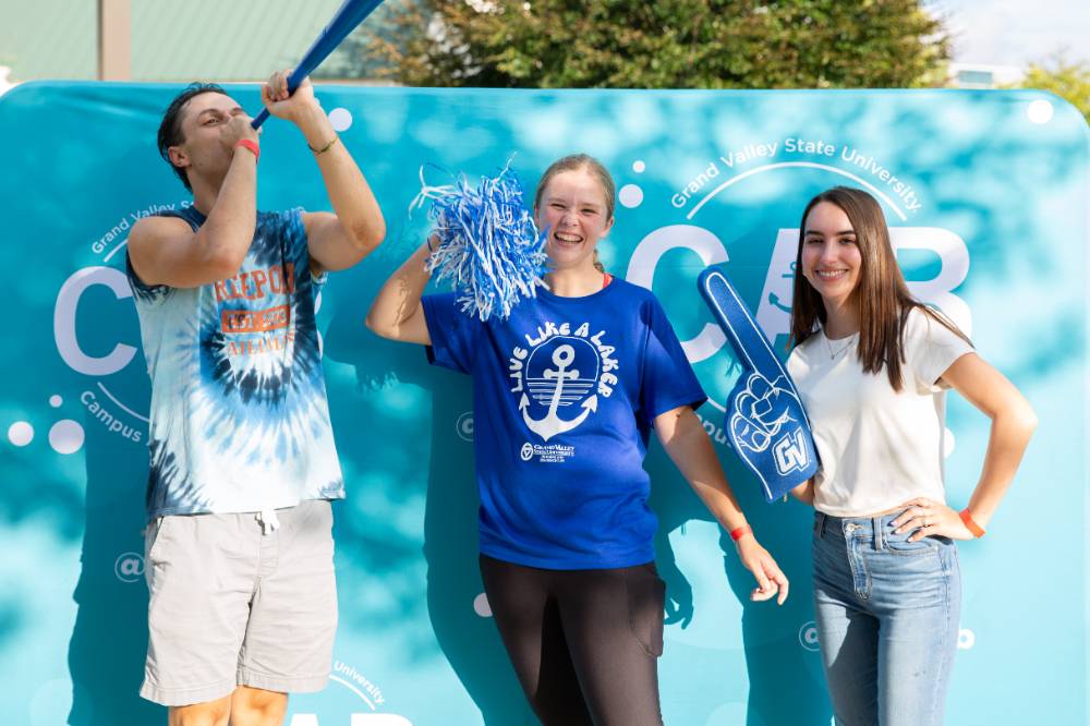 students posing in front of CAB backdrop at Laker Kickoff photo booth with horn and pom pom